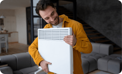 Man smiling while holding electric heater indoors.