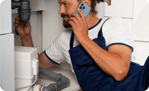 Plumber on phone inspecting under-sink pipes