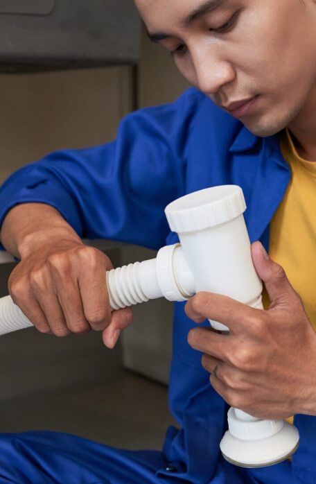 Plumber assembling white plumbing pipe under sink.